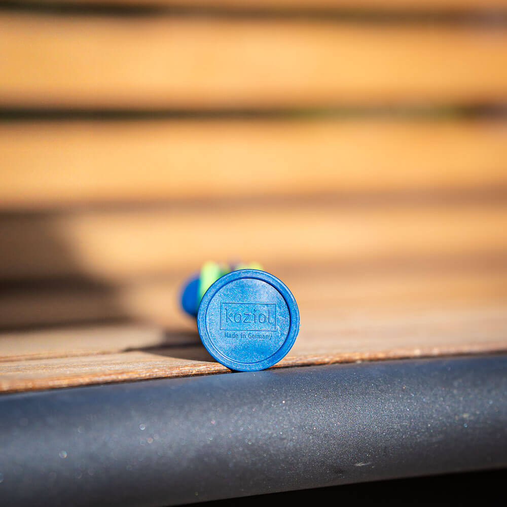 Made in Germany: Detail van duurzaam bestek Close-up van de onderkant van een blauw stuk bestek dat op een houten bankje ligt. De onderkant toont het logo "Koziol Made in Germany."