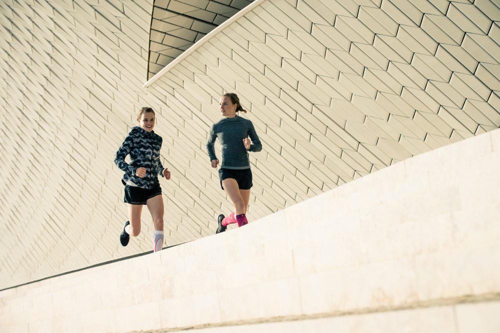 Twee lopers rennen naast een moderne muur in de stedelijke omgeving en praten