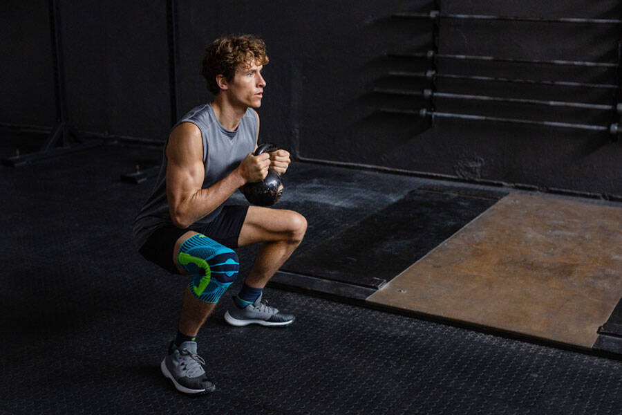 Man met een kneebord gaat diep gehurkt met een kettlebell tussen de twee handen