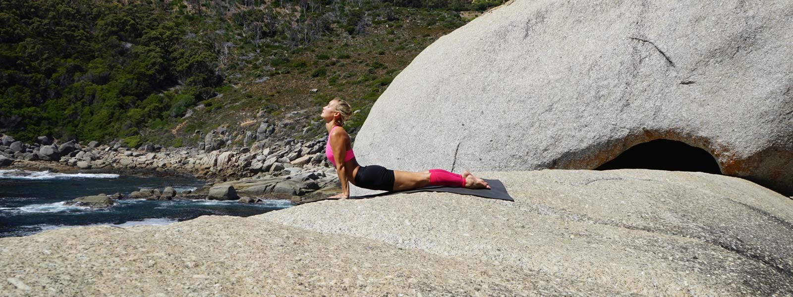 Vrouw doet yoga -oefeningen op een grote rots op het water en roze mouwen in de onderbeen