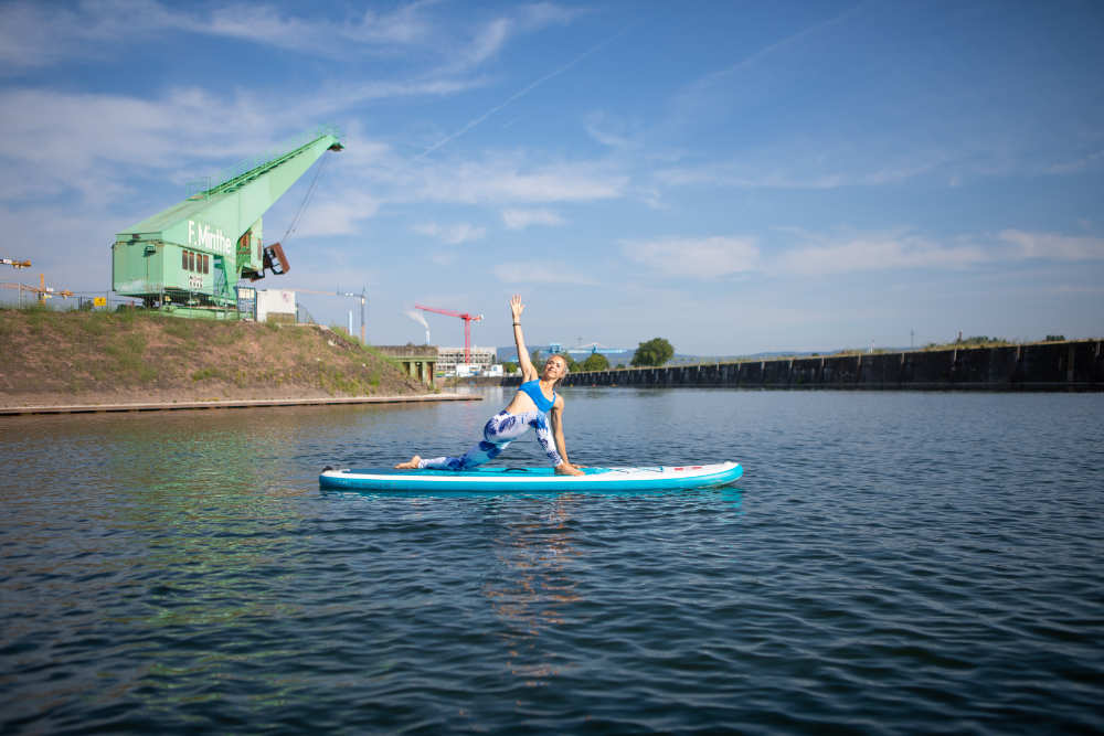 Sup yoga - laat gewoon los Vrouw maakt yoga -oefening op het bord met kranen op de achtergrond