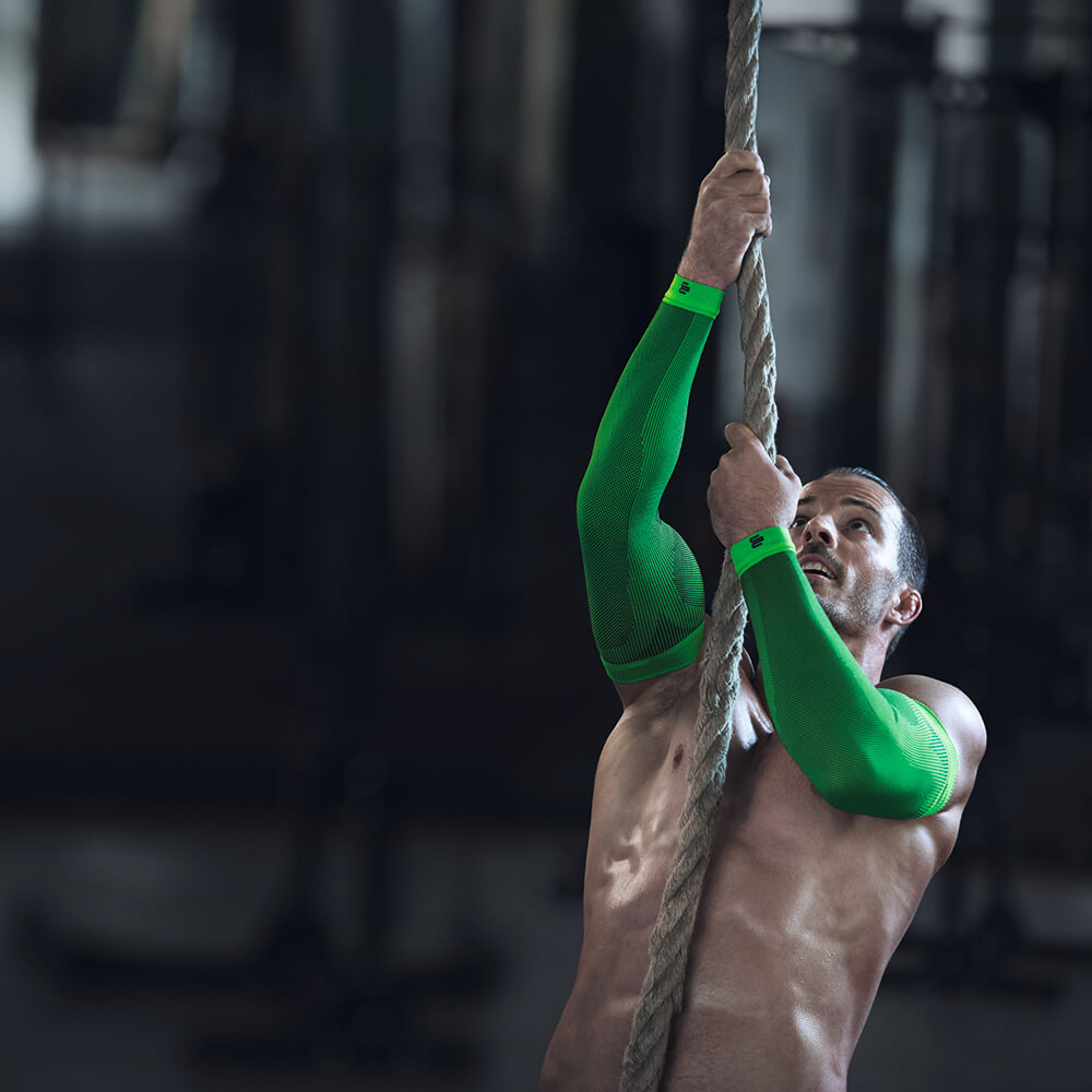 De man die een touw klimmen draagt	 draagt ​​groene compressiemouwen voor de arm
