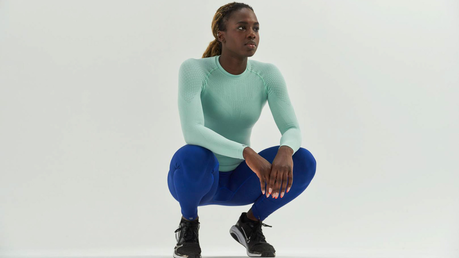 Athleet in mintgroen compressieshirt en blauwe compressiebroek in een hurkpositie voor een witte achtergrond.