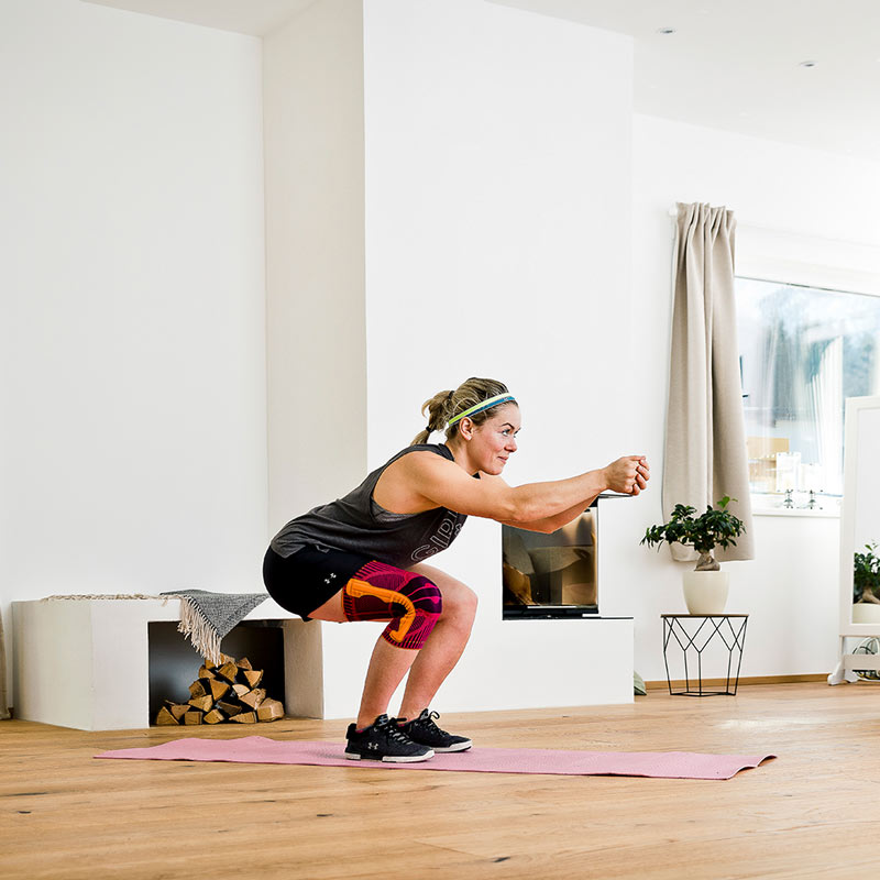 Ski -gymnastiek - de downhill -krat met sportkniesteun Vrouw met een knuppel simuleert de ski -afstammelingspositie in een open haardkamer, rechte armen gaan vooruit met ondervraagde handen