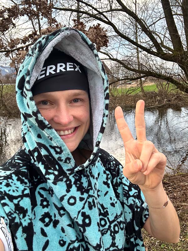Anna Hahner na het ijsbaden met Terrex-muts Anna Hahner in een Terrex-muts en kleurrijke poncho, handdoek om haar schouders gewikkeld, toont het vredesteken.