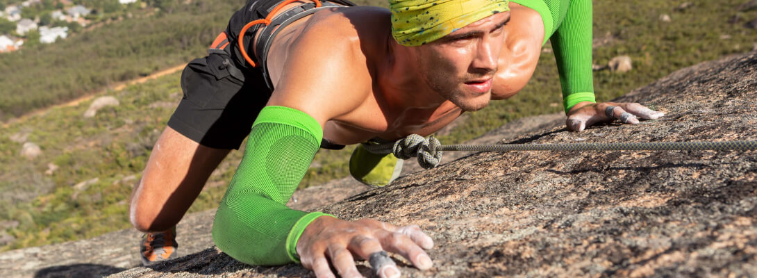 De klimmer op de rots draagt ​​groene compressiemouwen voor de arm
