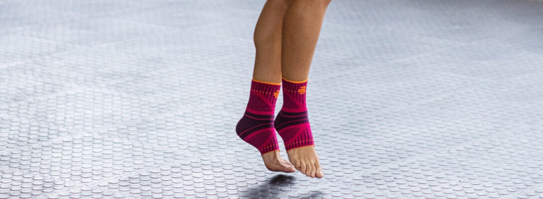 Zoom op de benen van een vrouw draagt ​​de sportbanden voor de enkel	 ze staat op de uiteinden van de teen op een grijs oppervlak
