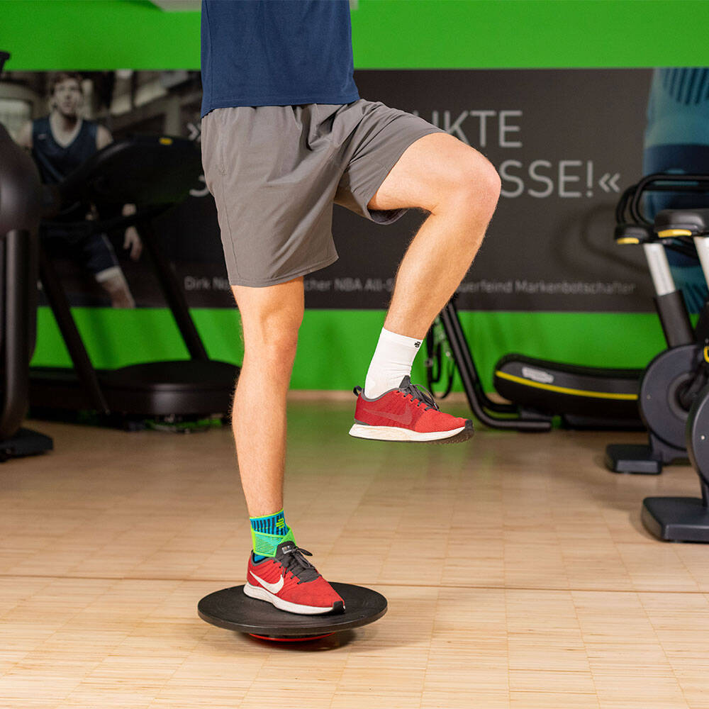 Man in een sportschool in balans met zijn rechterbeen op een balanskussen en draagt ​​een enkelband