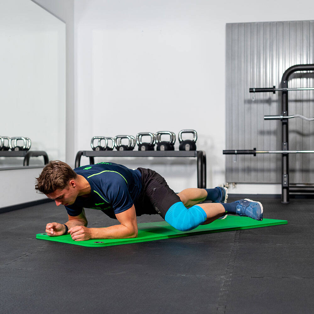 Man in de sportschool beweegt zijn linkerknie naar voren bij een onderarmplank