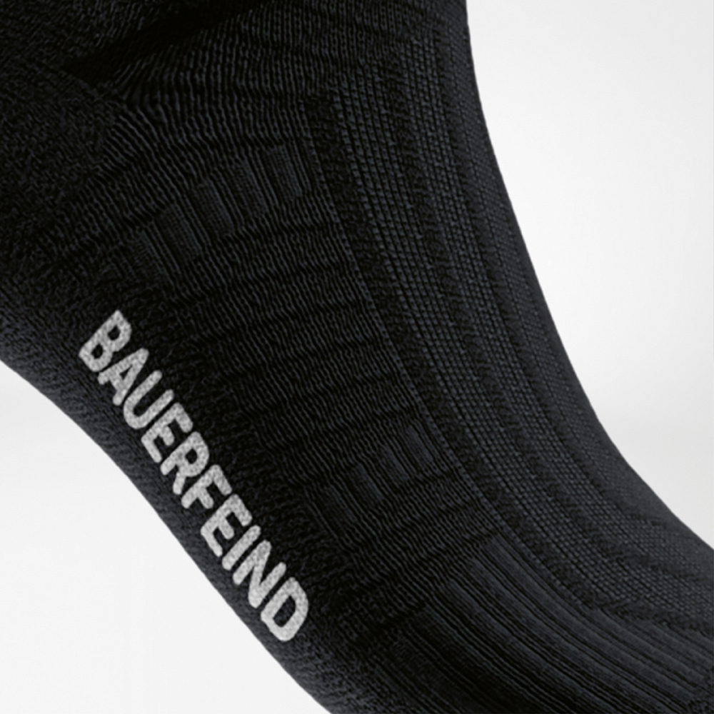 Close-up van de wreef van een zwarte compressie-hardloopsok met ingebreid BAUERFEIND-logo en gestructureerd oppervlak voor optimale grip.