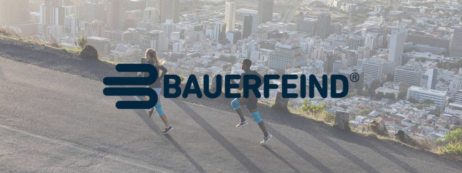 Bauerfeind: Beweging is ons DNA Bauer vijandelijke belettering op een foto waar twee lopers op een berg over de stad lopen