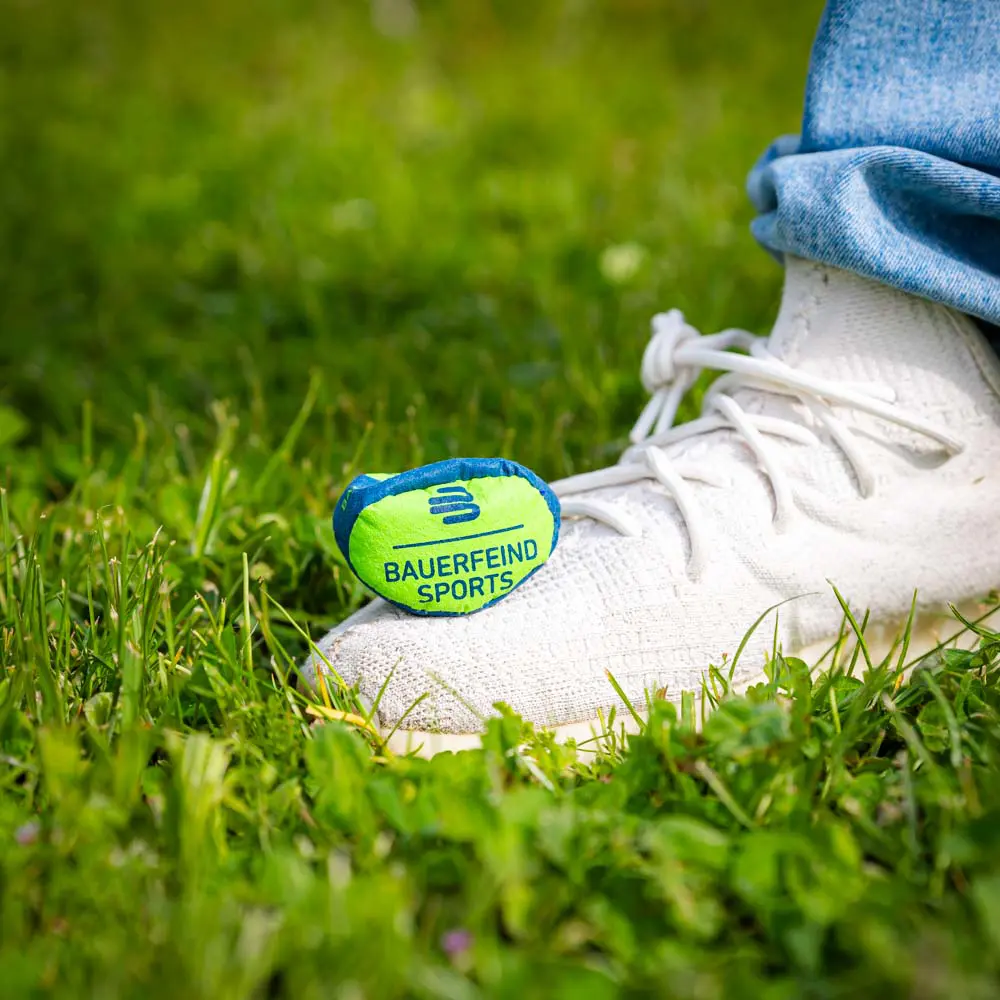 Kleine trainingsbal op gras Kleine Bauerfeind Sports bal op gras, geplaatst naast een witte schoen.