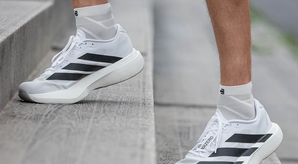Stap voor stap omhoog Close-up van witte hardloopschoenen met zwarte strepen en witte compressiesokken, gedragen tijdens het traplopen. De sokken reiken boven de enkel en bieden steun en comfort tijdens de training.