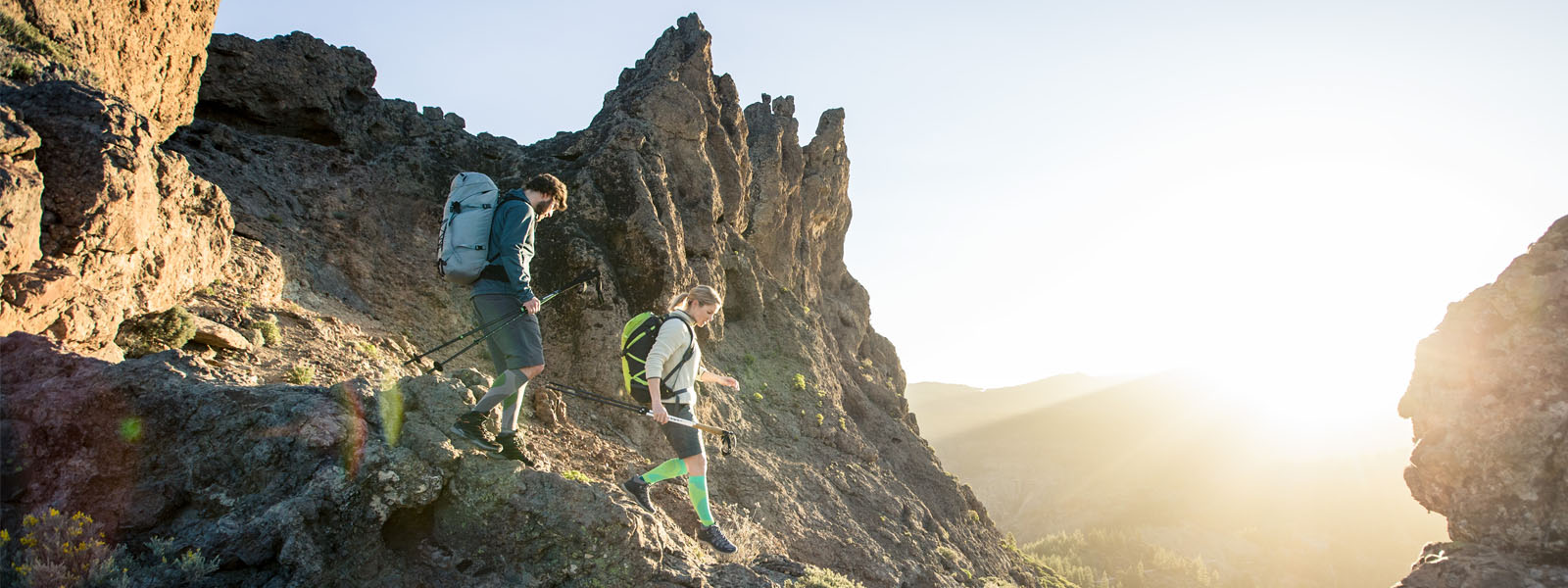 Wandel vreugde tot zonsondergang: onze outdoor performance compressiesokken Twee wandelaars met lange wandelsokken gaan een steil pad af op een berg aan schemering