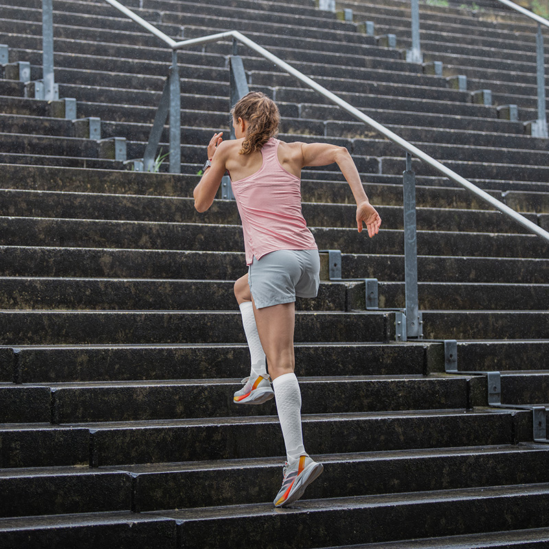 Onze runprestatiescompressiesokken geven je bijna vleugels bij Urban Running Vrouw rent door een stad met haar voeten in de lucht en draagt witte lopende sokken