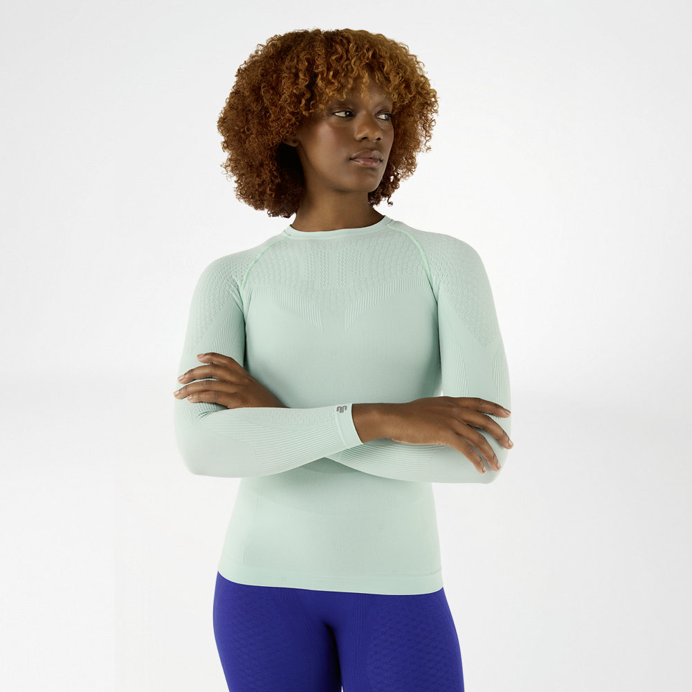 Vrouw in een lichtgroen, nauwsluitend langmouwshirt met gekruiste armen, vooraanzicht