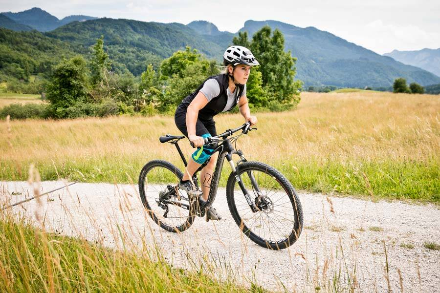 Vrouw met een kneebord rent op haar mountainbike over een grindpad tussen weiden en velden