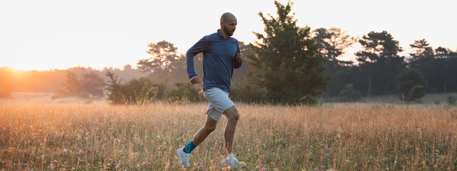 Achilles peespijn tijdens het hardlopen kondigt het gevecht aan - met onze ondersteuning van sport achilles Man met enkelverband loopt in schemering over een weide met een hoog gras