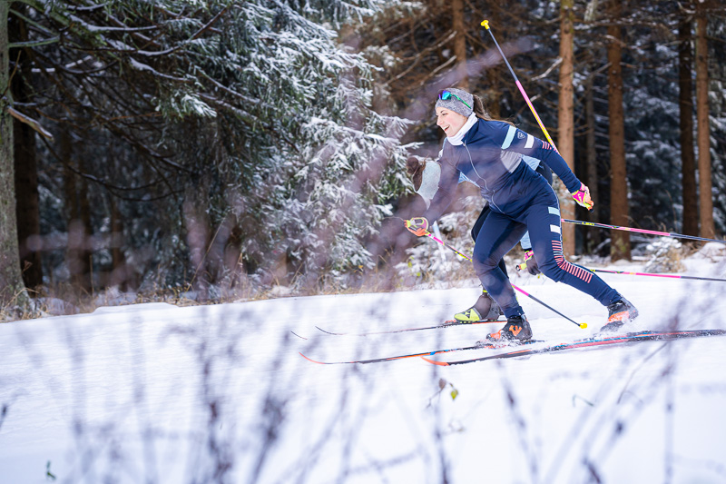 Dynamiek en precisie bij langlaufen door het besneeuwde bos. Een atlete die door een besneeuwd bos skiet. Ze beweegt energiek door diepe sneeuw, uitgerust met professionele ski-uitrusting en moderne sportkleding.