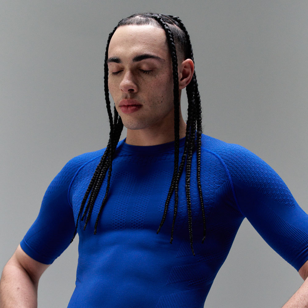 Een man met vlechten draagt een donkerblauw sporttopje, dat zijn spieren sterk benadrukt