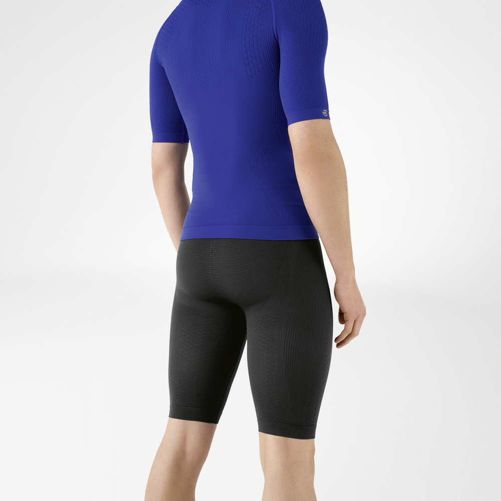 De man draagt een nauwsluitend blauw shirt dat zijn bovenlichaam benadrukt en een knielange, marineblauwe, nauwsluitende sportbroek die zijn onderlichaam omhelst.
