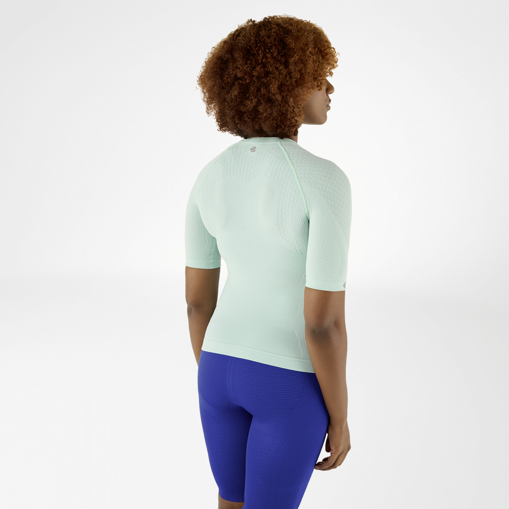 Stijlvol en Fit: Mintgroen Compressieshirt en Blauwe Leggings voor Haar Achteraanzicht van een vrouw met krullend haar in een mintgroen compressieshirt en blauwe leggings, die lichtjes opzij kijkt.
