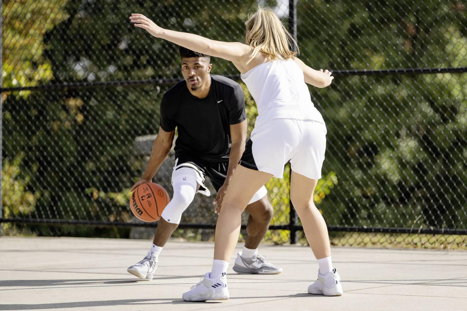 Streetball -speler met witte knie mouw probeert langs een tegenstander te komen die op hem wacht met de armen verspreid