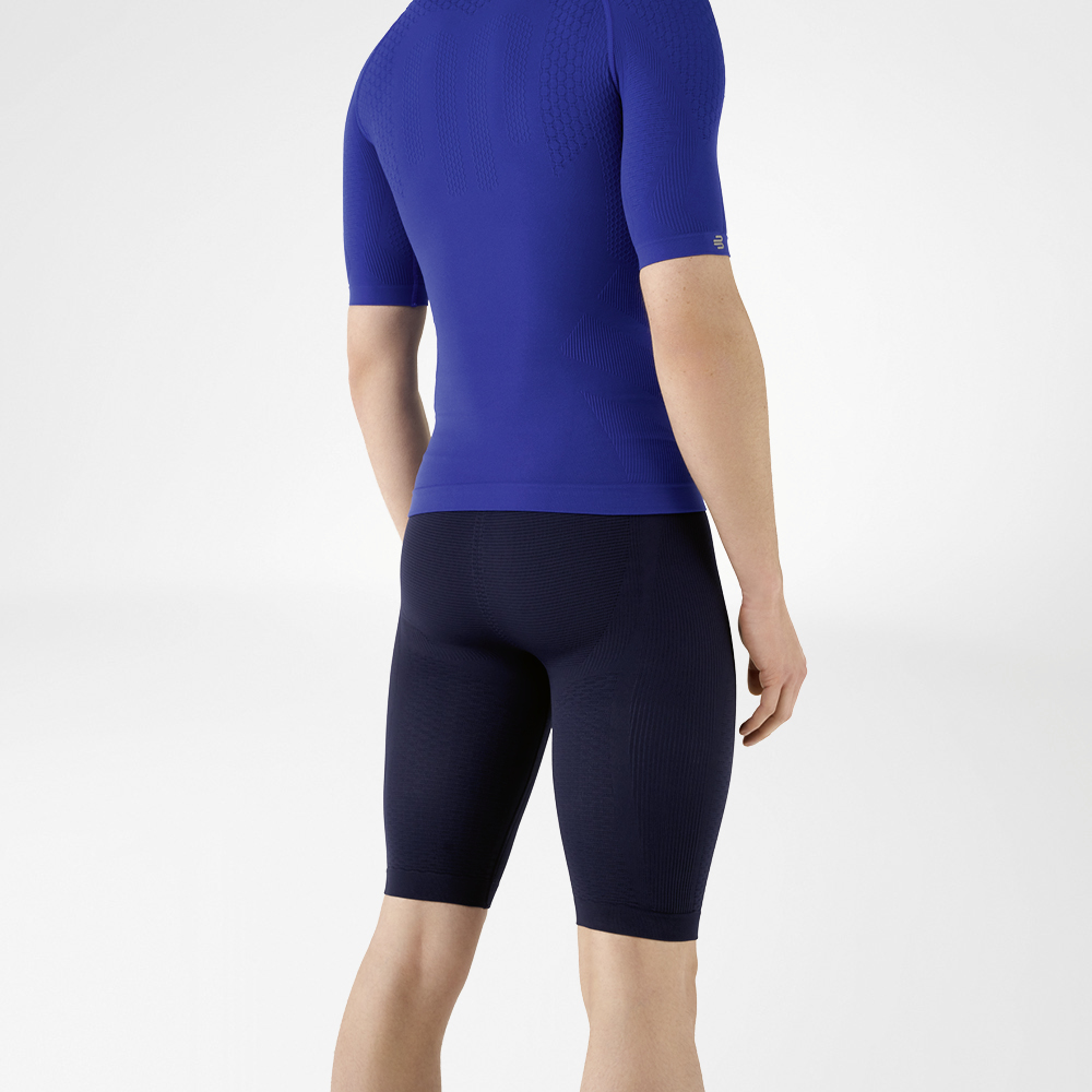 De man draagt een nauwsluitend blauw shirt dat zijn bovenlichaam benadrukt en een knielange, marineblauwe, nauwsluitende sportbroek die zijn onderlichaam omhelst.