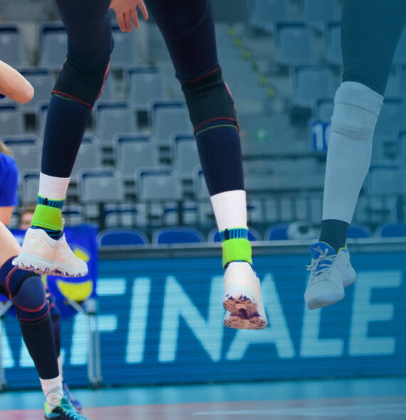 Volleybalspeler met donkere broek	 witte schoenen en blauwe enkelbanden "Stands" in de lucht