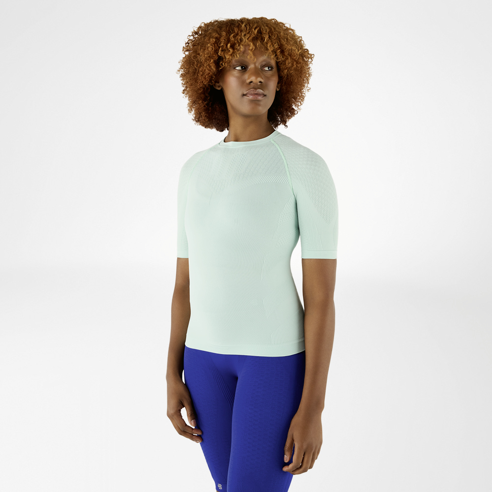 Vrouw in een mintgroen compressieshirt en blauwe leggings, naar voren gericht.