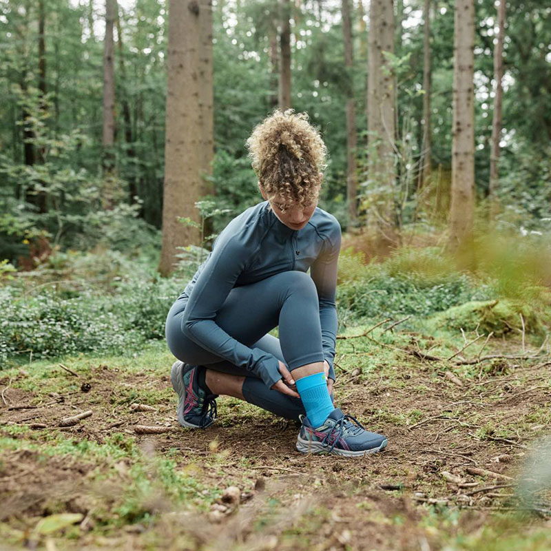 Een hardloopster knielt op de grond in het bos en maakt haar achillespeesverband in orde