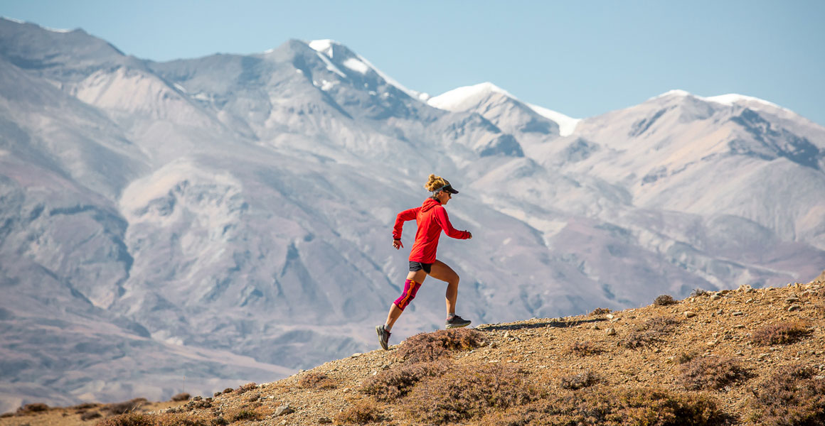 Trailläriner rent op met de Himalaya op de achtergrond en draagt ​​een kniestanding