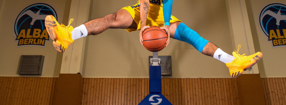 Basketbalspeler maakt een evenwichtsoefening. Hij draagt ​​een kniehuls op het linkerbeen