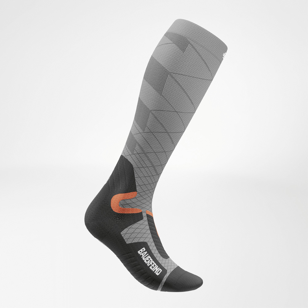 Grijze skisok met compressie voor dames in zijaanzicht, met anatomisch geoptimaliseerde pasvorm en sportief ontwerp met oranje en zwarte accenten.
