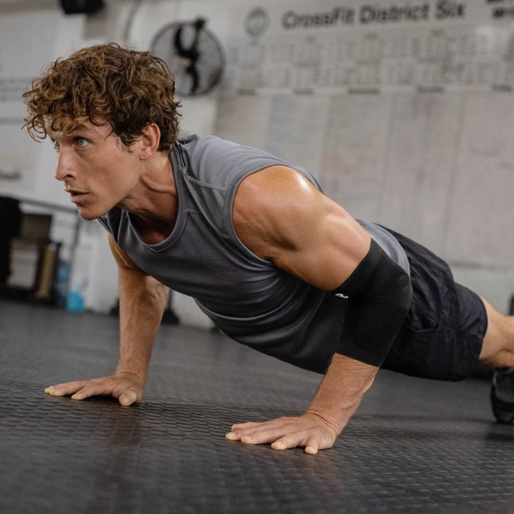 Een atleet in de sportschool die een intense push-up workout uitvoert, met een zwarte elleboogbrace. De brace biedt stabiele ondersteuning en optimale bescherming voor de elleboog tijdens krachttraining en sportieve uitdagingen.