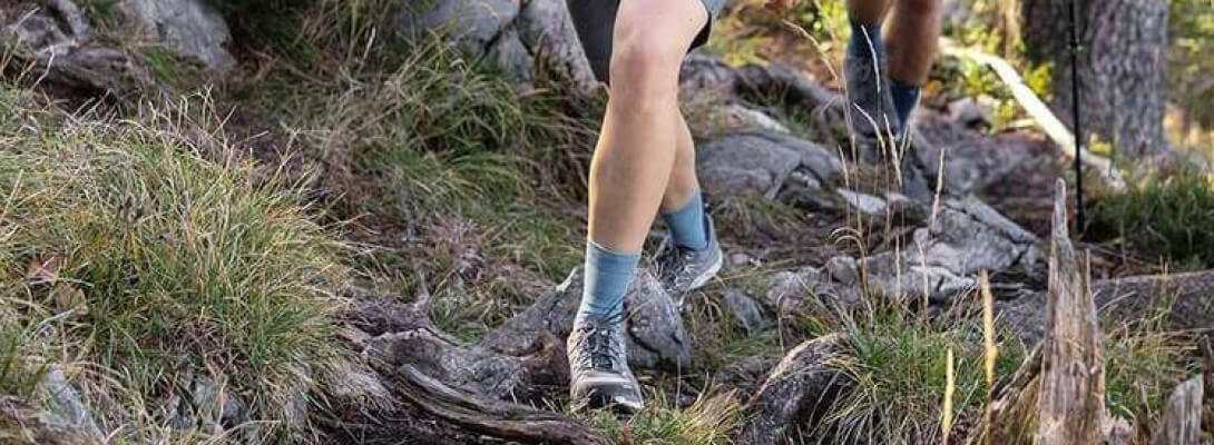 Merino-wandelsokken van middellange lengte tijdens het wandelen in het bos Zwante vrouw op een steenachtig oppervlak draagt middellange wandelsokken