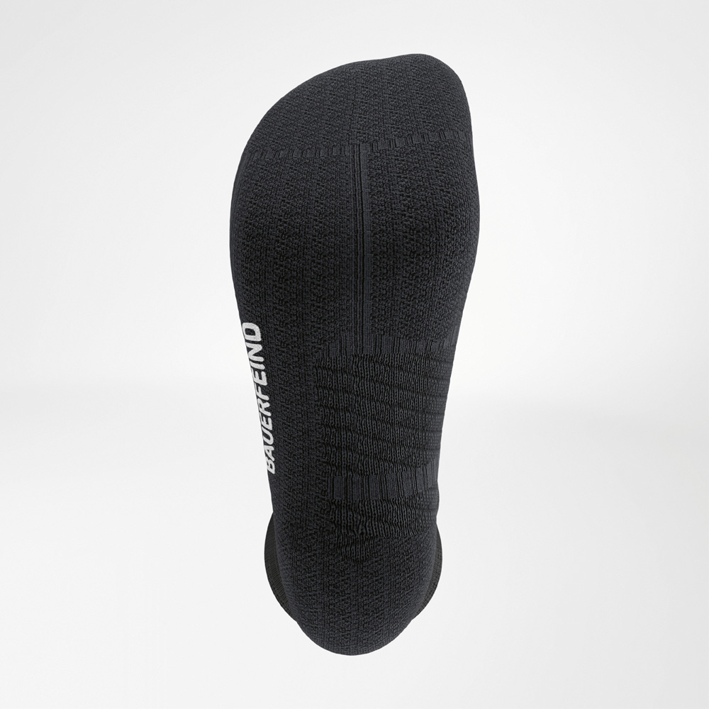 Detailopname van de zool van een zwarte hardloopsok met dempende structuur, ergonomische naden en BAUERFEIND-logo aan de zijkant.