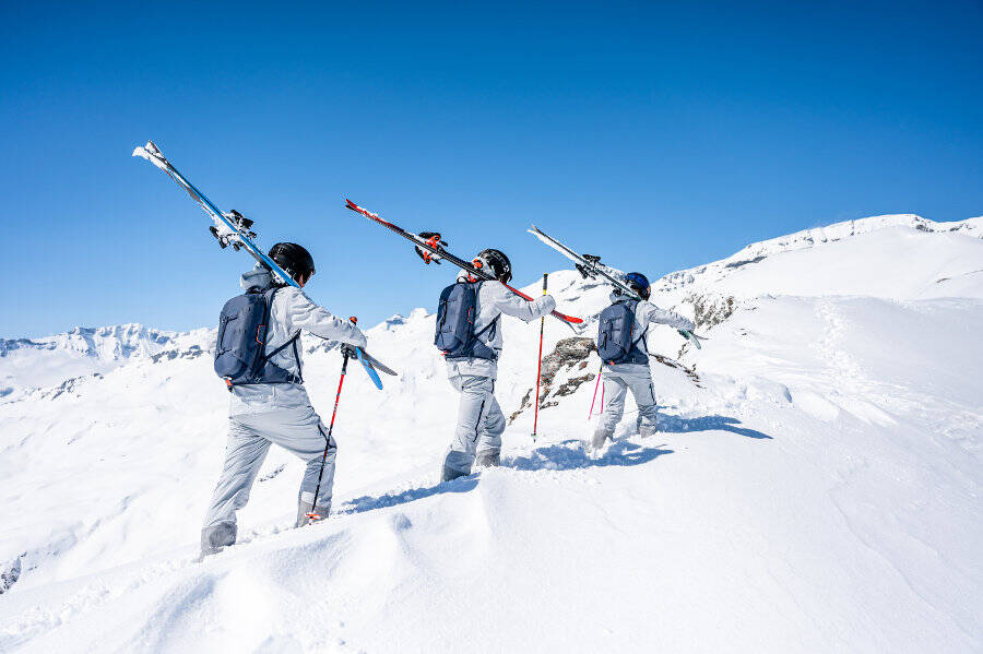Drie skiërs dragen hun ski's op hun schouders door diepe sneeuw op een berg