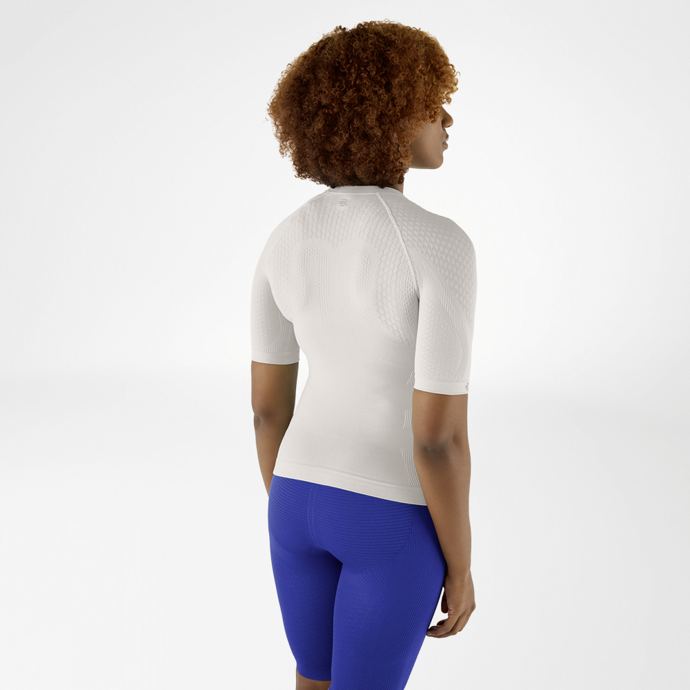 Achteraanzicht van een vrouw met krullend haar in een zilvergrijs compressieshirt en blauwe leggings, die lichtjes opzij kijkt.