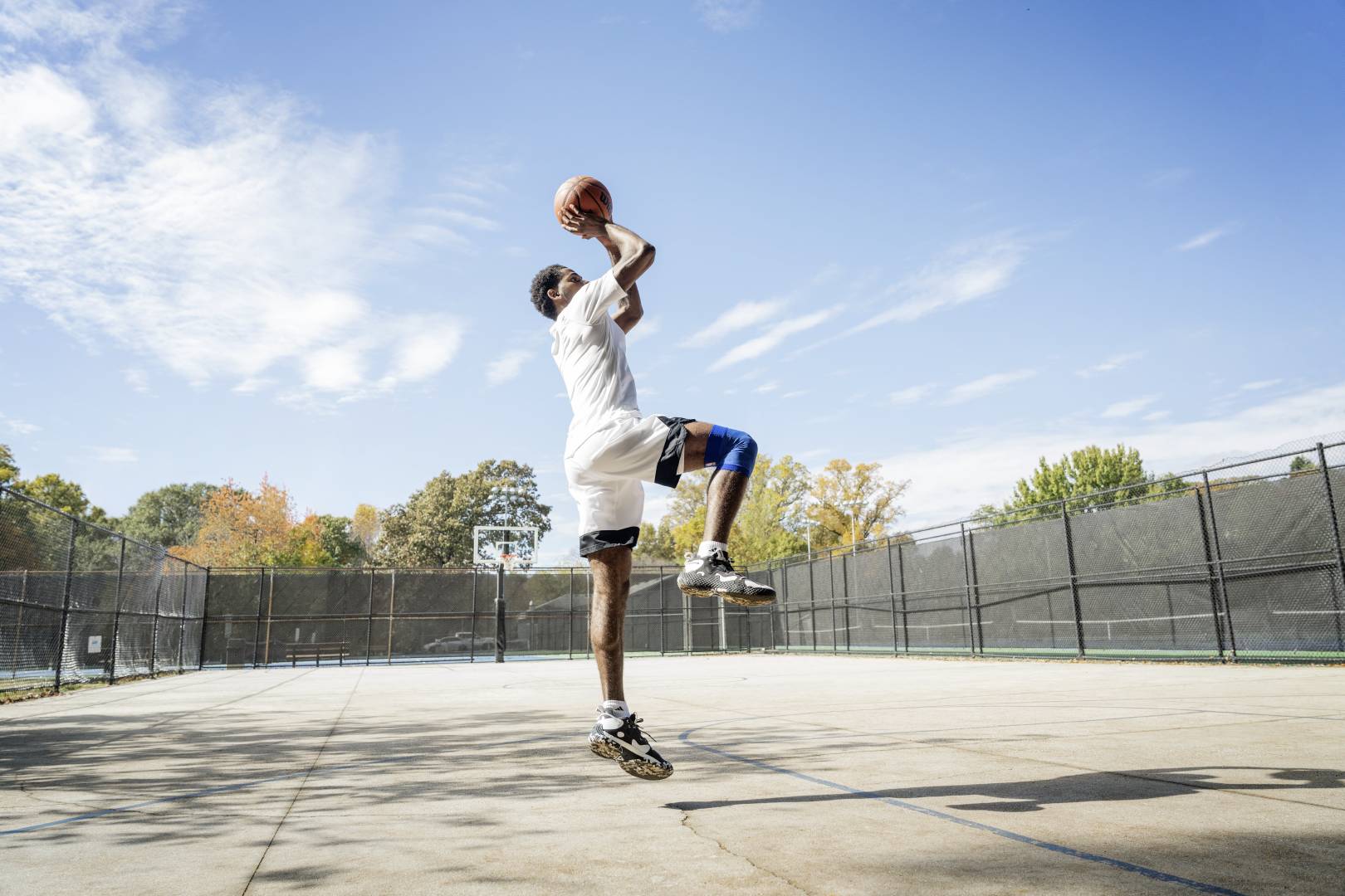 Basketbalspelers springen op een straatveld voor de worp uit handen met de bal over het hoofd, gebogen in de andere, laten de andere verticaal naar beneden zien