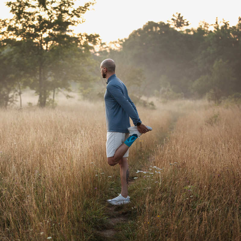 De man strekt zich uit bij zonsopgang op een weide met een hoog gras